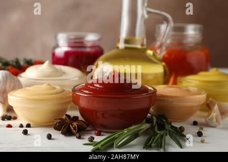 Set of different delicious sauces, olive oil, garlic, tomato cherry on white table against brown background, closeup Stock Photo