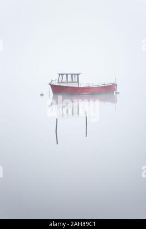 Leisure boat in the mist on an early Autumn morning just after sunrise on Coniston Water in the Lake District, Cumbria, England. Stock Photo