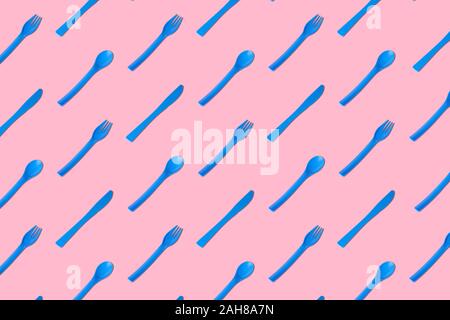 Flat lay of blue plastic disposable forks,spoons and knives pattern on pastel pink background minimal creative concept. Stock Photo