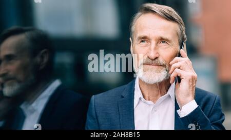 Serious bearded businessman talking on a mobile phone while standing outdoors Stock Photo
