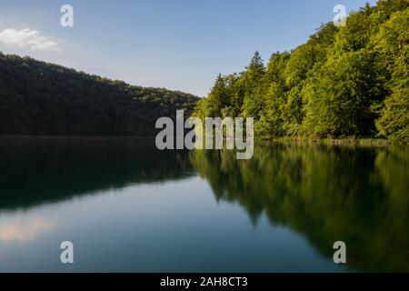 Symmetrical wide angle view of a croatian lake in the late afternoon light, with trees reflecting on water Stock Photo