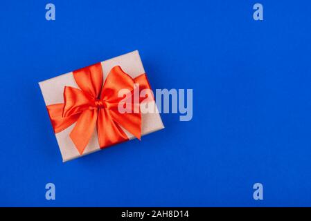 Cardboard gift box with red bow on blue background. Stock Photo
