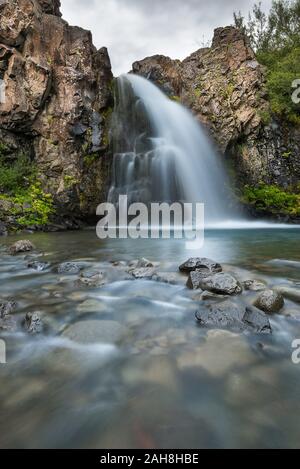 Low angle view of an icelandic waterfall flowing out of the rock and into a crystal clear pond Stock Photo