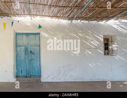 Blue wooden door, small window and straw roof with dramatic light rays and shadows at abadoned church Ermita de Sant Antoni y Sant Jaume in Cap Blanch Stock Photo