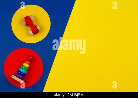 Baby kids toys background. Wooden stacking pyramid tower and red toy car on round yellow and red frames above navy blue background Stock Photo