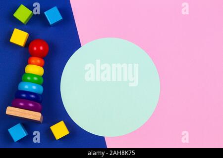 Baby kids toys wooden stacking pyramid tower and wood bricks on pink and blue navy background with blank round light green frame for text or image Stock Photo