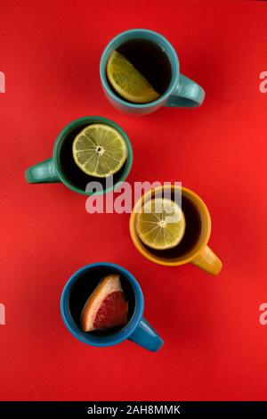 Many mugs of tea and citrus fruits on a red background, top view. Lemon, pomelo, orange, citrus Sweetie, grapefruit. Stock Photo