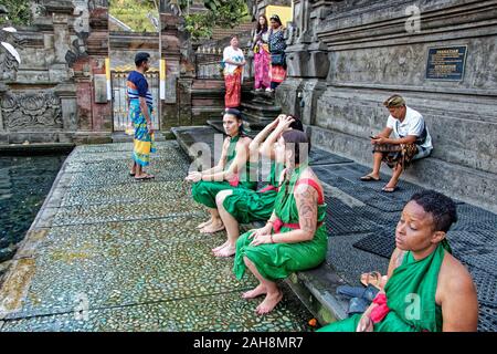 Women in green fabric clothes sitting on the edge of sacred pool i Tirta Empul Temple on Bali Stock Photo