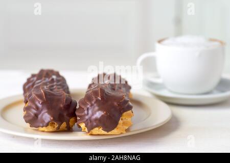 Two eclairs and cup of cappuccino on white wooden table Stock Photo