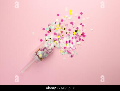 Popper with multi-colored paper confetti on a pink background. Stock Photo
