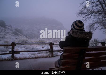 Person sitting in the winter cold outside on a bench. Model posing for a concept of homeless. Stock Photo