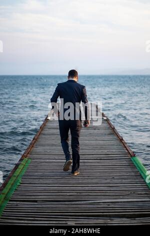 man in suit walking in a port on the way to the sea next to the end Stock Photo