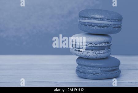 Orange and blue macaroons on yellow background, French cookies as a treat for the holiday, toned trendy classic blue color of year 2020 Stock Photo