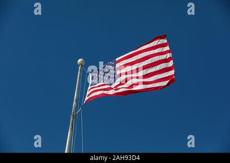 Looking up at large, new United States of America flag flying in the wind on a sunny day with deep blue sky in background Stock Photo