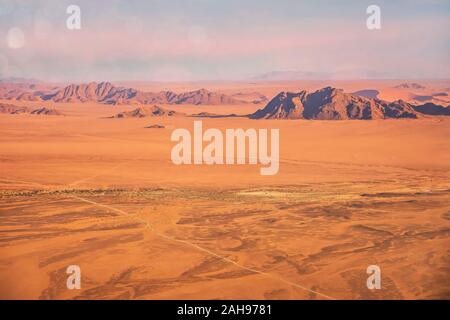 Aerial view of the dramatic landscape of the Namib Desert, showing long straight roads running through desolate terrain. Sossusvlei, Namibia. Stock Photo
