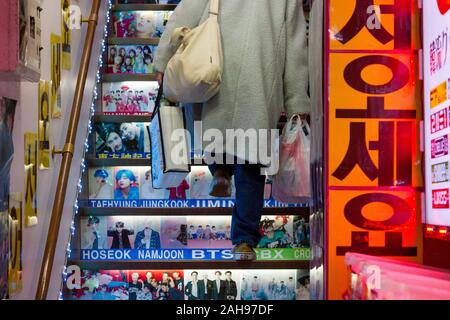 A woman carrying shopping bags climbs stairs with pictures of Korean idols and celebrities on them in a shop in Shin-Okubo, Shinjuku, Tokyo, Japan. Stock Photo