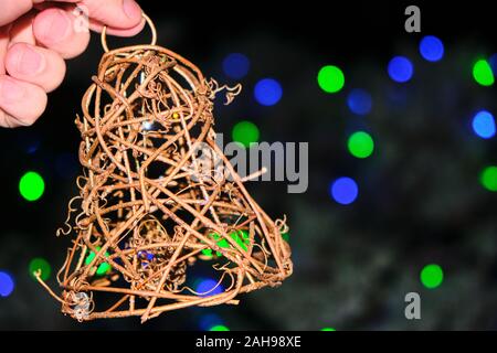front photo of a handmade bell made of wicker, held by a hand of a young Caucasian man with a background of unfocused colored lights and a free space Stock Photo