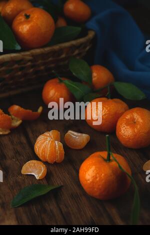 Mini tangerines with leaves in a basket and on a wooden table. Vertical photo in low key. Stock Photo