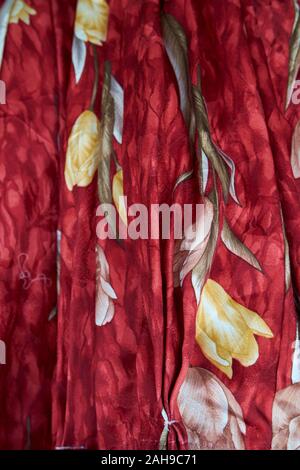 At a textile, fabric stall, plenty of styles from which to choose. Here, various shades of red with flowers. In Tawau, Sabah, Borneo, Malaysia. Stock Photo