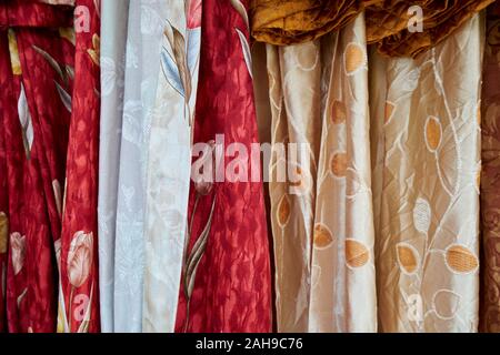 At a textile, fabric stall, plenty of styles from which to choose. Here, various shades of red and gold with flowers. In Tawau, Sabah, Borneo, Malaysi Stock Photo