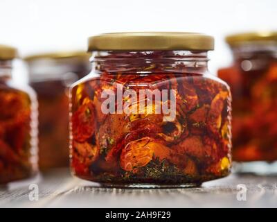 Home-made canned red dried cherry tomatoes are packed in small glass jars. Stock Photo