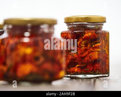 Home-made canned red dried cherry tomatoes are packed in small glass jars. Stock Photo