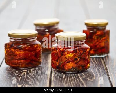 Home-made canned red dried cherry tomatoes are packed in small glass jars. Stock Photo