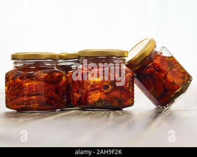 Home-made canned red dried cherry tomatoes are packed in small glass jars. Stock Photo