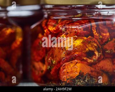 Home-made canned red dried cherry tomatoes are packed in small glass jars. Stock Photo