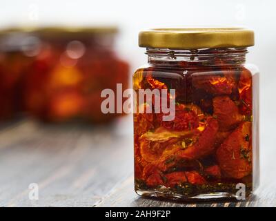 Home-made canned red dried cherry tomatoes are packed in small glass jars. Stock Photo