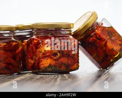 Home-made canned red dried cherry tomatoes are packed in small glass jars. Stock Photo