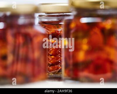 Home-made canned red dried cherry tomatoes are packed in small glass jars. Stock Photo