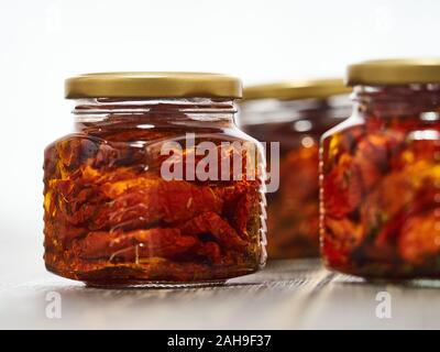 Home-made canned red dried cherry tomatoes are packed in small glass jars. Stock Photo