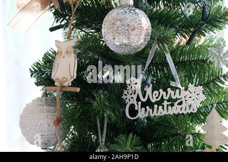 December 2019 - White and silver Christmas decorations hang on a traditional, artificial green Christmas tree Stock Photo