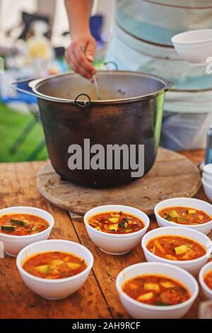 Man pouring vegetables stew from a pot into bowls. Cooking food in nature. Stock Photo