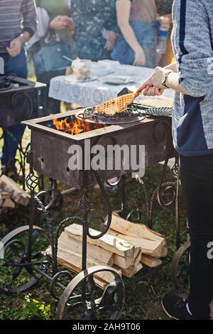 Baking waffles on open flame outdoors in a hammered cast iron grill. Defocused background of people waiting for waffles. Stock Photo