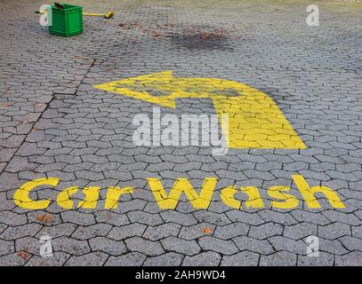 Washed-out old ugly painted yellow entry sign for a car wash on a dirty old pavement of a petrol station Stock Photo