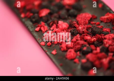 Dark low calorie chocolate with dried red berries on bright pink background, selective focus Stock Photo