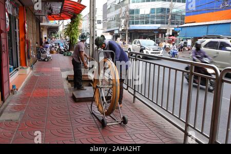 Bangkok,Thailand-December 26, 2019:Blurred motion of a worker rolling cable reel while the other holding and inserting the cable into underground pipe Stock Photo