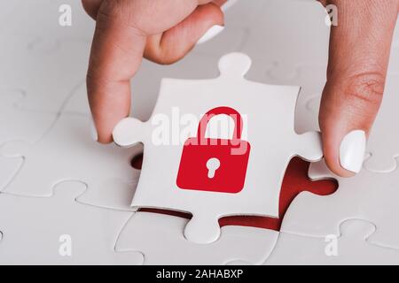 close up of woman holding white jigsaw with red padlock near connected puzzle pieces Stock Photo