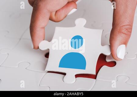close up of woman holding white jigsaw with blue human icon near connected puzzle pieces Stock Photo