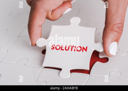 close up of woman holding white jigsaw with solution lettering near connected puzzle pieces Stock Photo