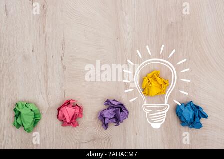 top view of multicolored crumpled paper balls and light bulb illustration on wooden surface, business concept Stock Photo