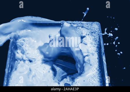 Blue splash after brush falling into fluid paint on black background. Scene toned in trendy classic blue - color of the year 2020 concept. Dynamic bac Stock Photo