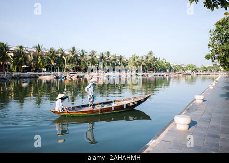 Around 2019, people dressed in traditional Vietnamese clothes are crossing the river in a boat. Stock Photo