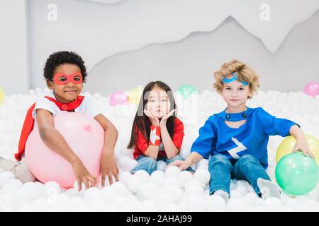 Adorable little intercultural friends in costumes playing in children room Stock Photo
