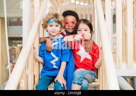 Three affectionate little friends in costumes playing on staircase together Stock Photo