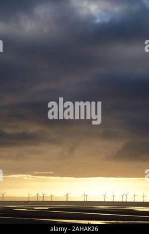 A row of offshore wind turbines beneath a cloudy stormy sky Stock Photo