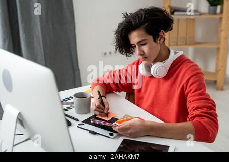 Young home office designer making notes and choosing color from palette Stock Photo