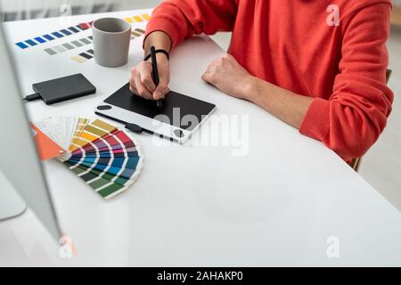 Hands of young freelance designer retouching photos on screen of graphics tablet Stock Photo
